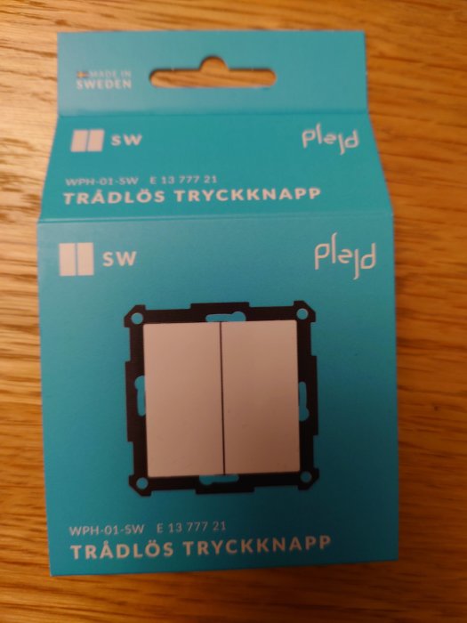 Förpackning för trådlös tryckknapp av märket Plejd, "Made in Sweden", blå färgsättning, produktinformation.