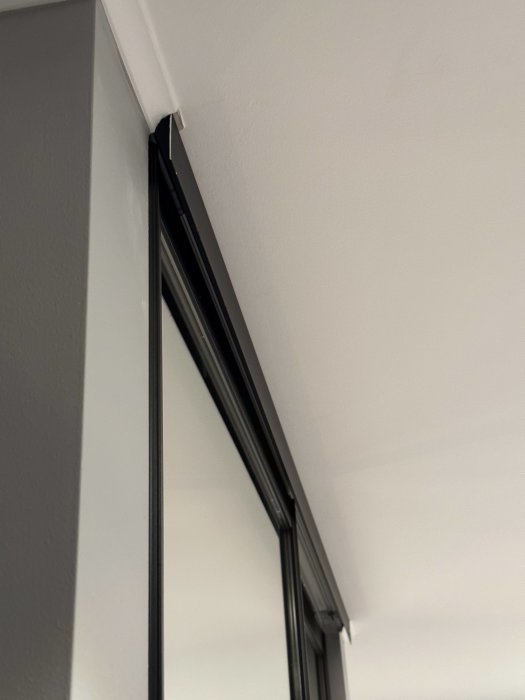Fönsterhörn i rum, grå väggar, vit tak, svart fönsterkarm, dagsljus, inomhus, arkitektonisk detalj.