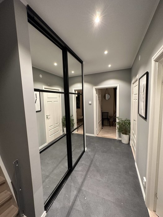Elegant korridor med grått golvt och vit dörr, svarta glasdörrar, inbyggda taklampor, modern inredning.
