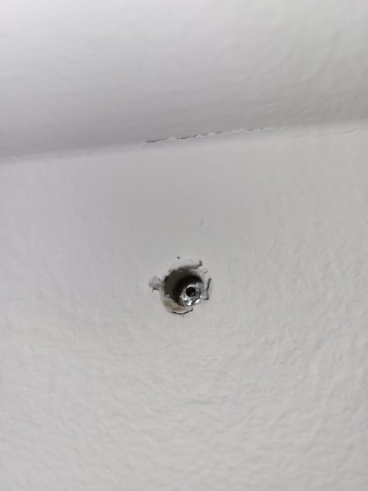 Ett hål i en vit vägg med en synlig plugg och skruv inuti.