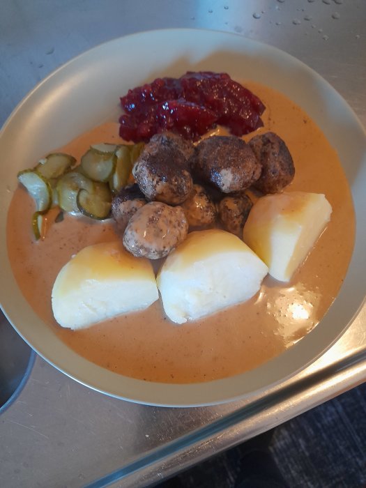 Köttbullar, potatis, brunsås, lingonsylt och inlagd gurka på en tallrik. Klassisk svensk maträtt.