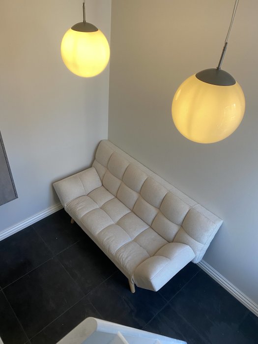 Modernt vardagsrumshörn med beige soffa och två pendellampor ovanför. Neutralt och minimalistiskt inrett.