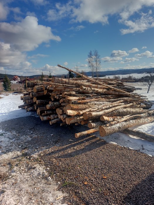 Trähögar i snötäckt landskap, blå himmel, delvis molnigt, röd hus i bakgrunden, flagnad snö på marken.