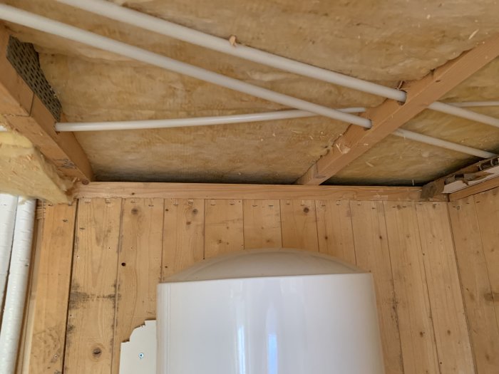 Takstoler og isolasjon sett nedenfra med rør lagt over treverk i et byggprosjekt.