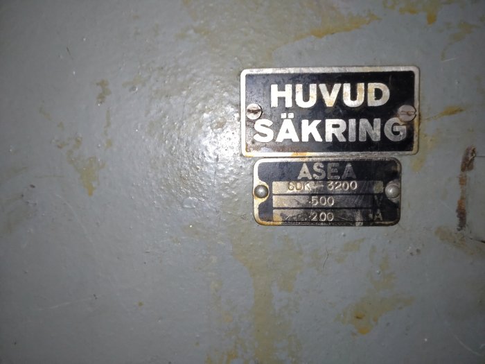 Två gamla skyltar på en sliten yta, märkta "HUVUD SÄKRING" och "ASEA", med elektriska specifikationer.