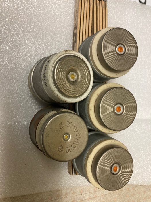 Fyra gråa använda filterpatroner ligger på vit skumplast nära brunt trallgolv.