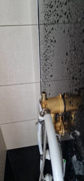 Inomhus VVS-installation, droppande vatten, spegelreflektion, kakelvägg, mässingsventil, flexibla slangar, våta ytor.