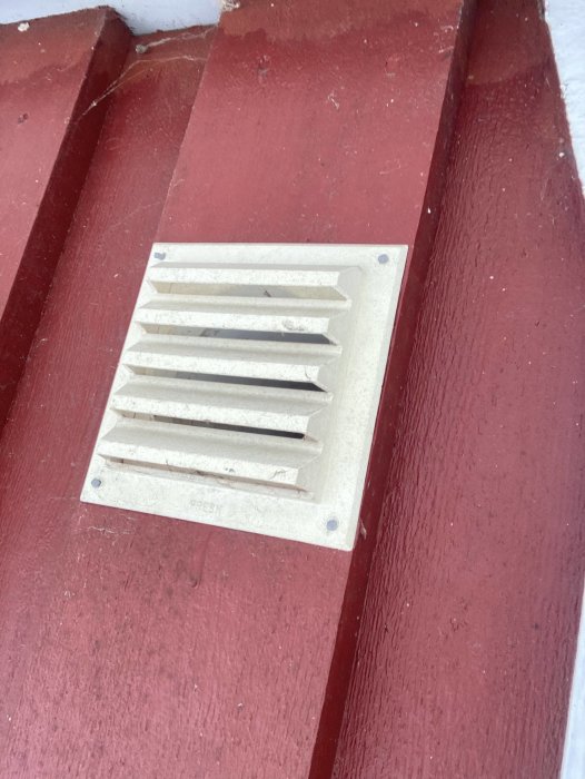 Ventilationsgaller på rödmålad vägg, ute på hus. Slitet utseende, behöver rengöras.