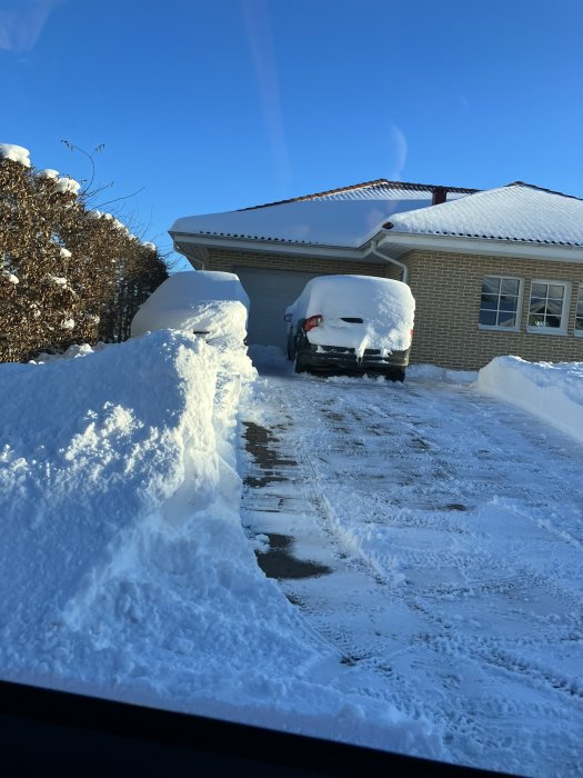 Ett snötäckt bostadshus och bil, klar himmel, vinterdag, snöskottad uppfart.