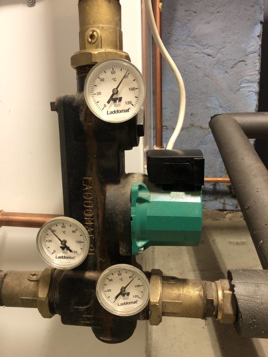 Värmesystem med pump, rör och tre tryckmätare mot en murad vägg.