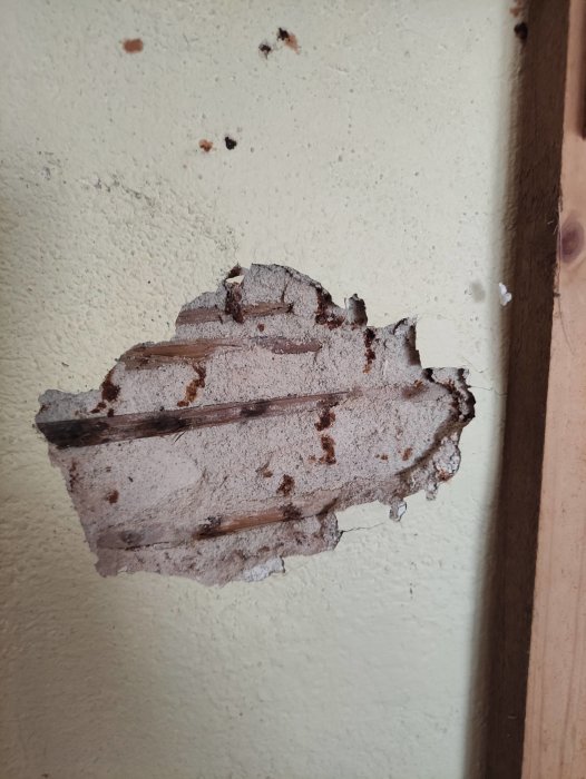 Vägg med flagnande gammal färg och synliga träreglar, skadad yta, underhåll behövs.
