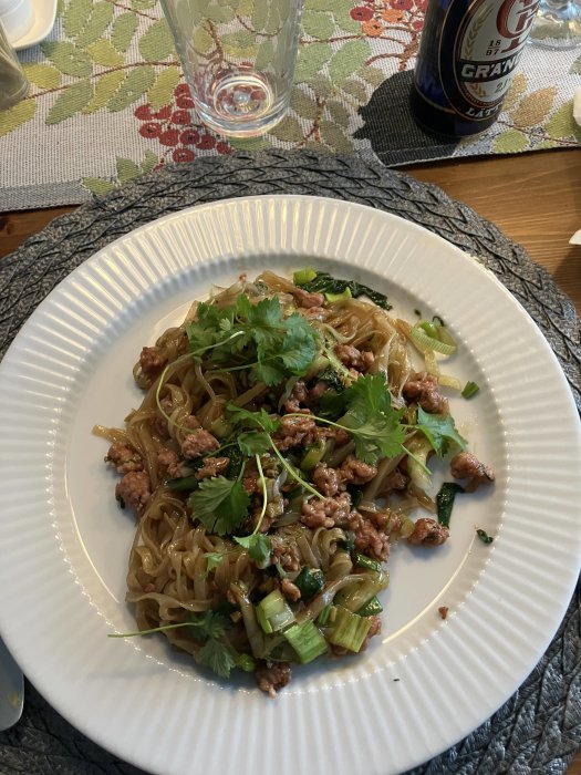 En tallrik med asiatiska nudlar, köttfärs, purjolök, koriander. En ölburk och ett tomt glas syns också.