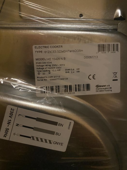 Etiketter på metallisk yta, detaljer om en elektrisk spis: modell, spänning, lastning, produktkod och CE-märkning.