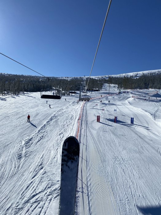 Skidlift, åkare, snötäckt bergslandskap, klarblå himmel, skidspår, skidort, vinteraktivitet, avslappnat, soligt väder.