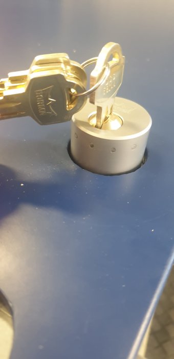 Nyckel insatt i ett runt lås ovanpå en blå yta med reflektioner.