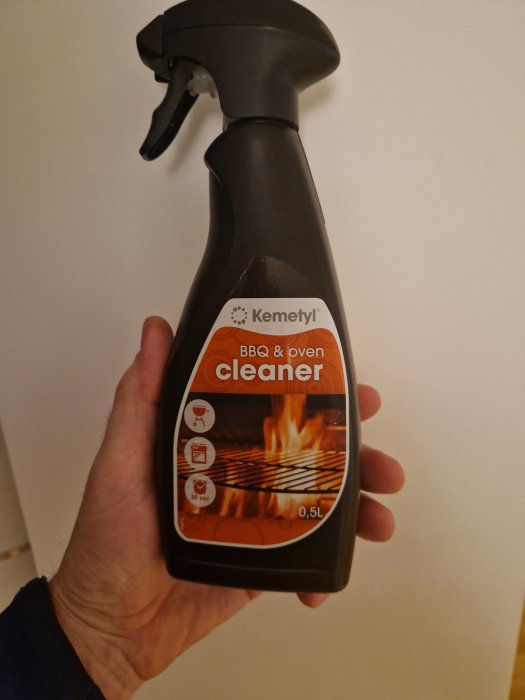 En hand håller en flaska med BBQ- och ugnrengöringsspray märkt "Kemetyl", halv liter.