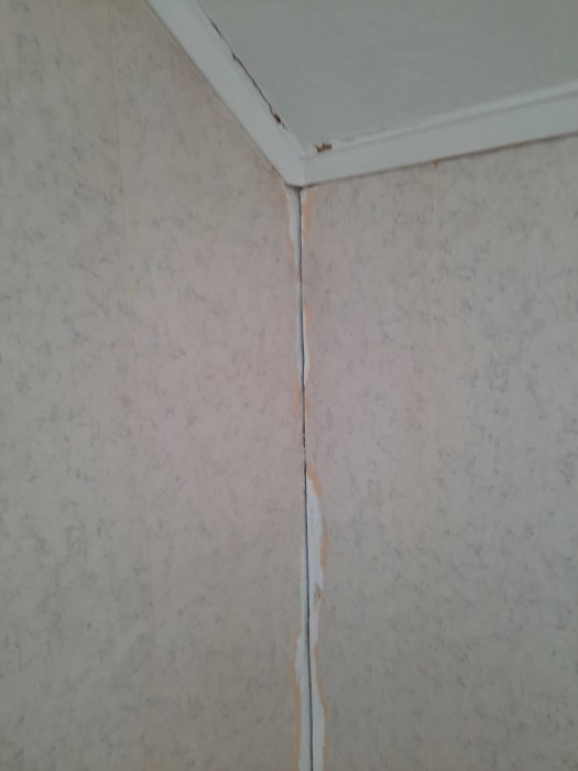 Hörnet av ett rum med spruckna och flagande tapeter, behov av renovering.