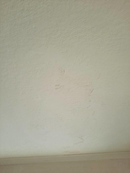 Vägg med fläckar och sprickor nära taket, behöver eventuellt renovering eller ommålning.