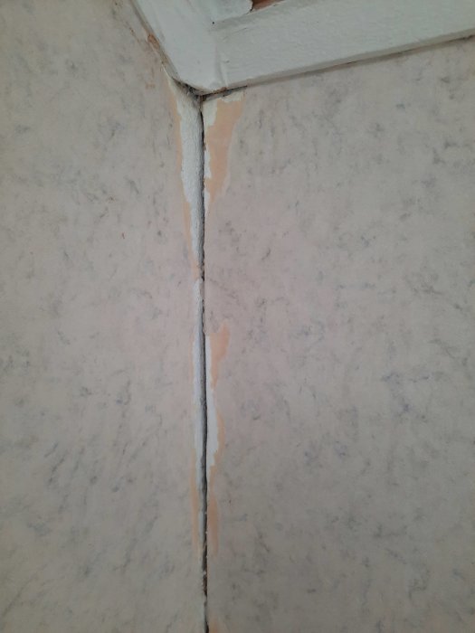 Vägg med skadad tapet och en spricka vid en hörna. Reparationsbehov synligt.