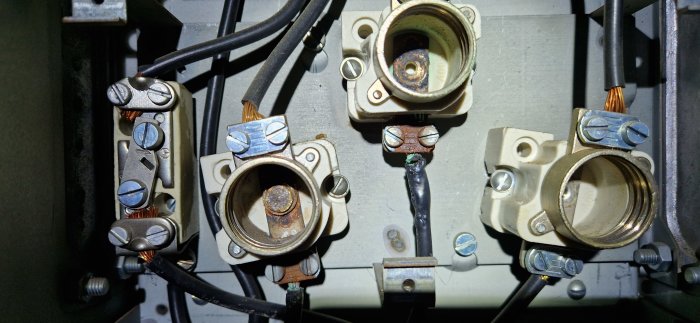 Gamla, rostiga eluttag och avskalade kablar i en elektrisk panel. Behöver underhåll eller utbyte.
