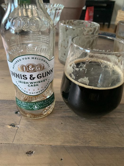 Tom ölflaska, delvis fylld ölglas, möjligtvis stout, på ett träbord.