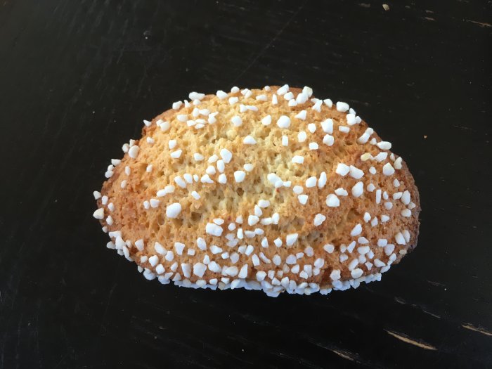 Gyllenbrunt bakverk med pärlsocker, ovalt, på mörk bakgrund.