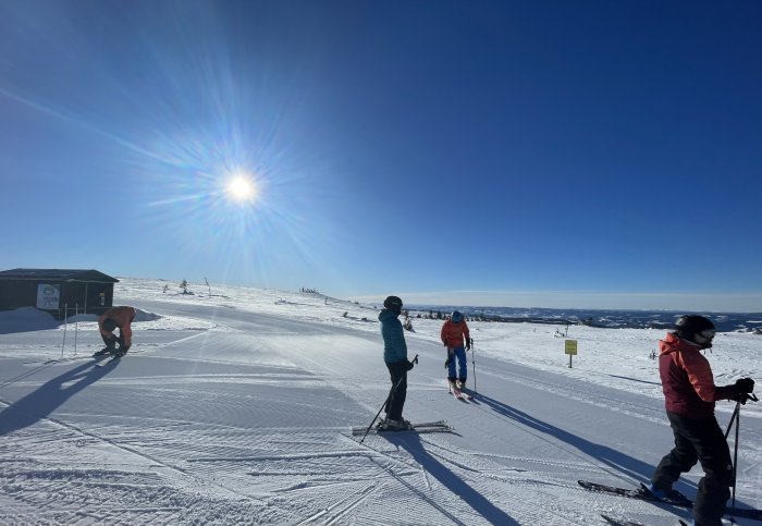 Skidåkare på snötäckt berg, klarblå himmel, strålande sol, vinterdag, skidlift, avkoppling, sport, friluftsliv, natur.