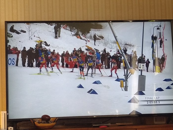 Längdskidåkning på TV, åkare i täten, publik, snöig backe, tävlingens slutvarv, tidtagning på skärm.