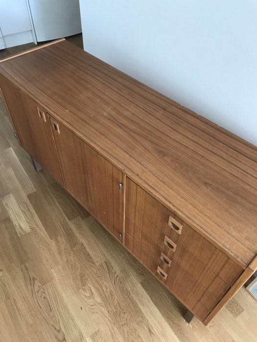 Träsideboard mot vit vägg, retro design, fyra lådor, två skåpdörrar, parkettgolv.