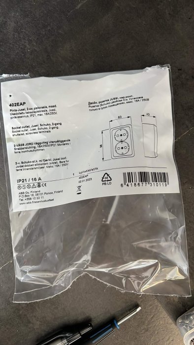 Transparent plastpåse med etikett för eluttag. Innehåller installationsschema och produktinformation på flera språk.