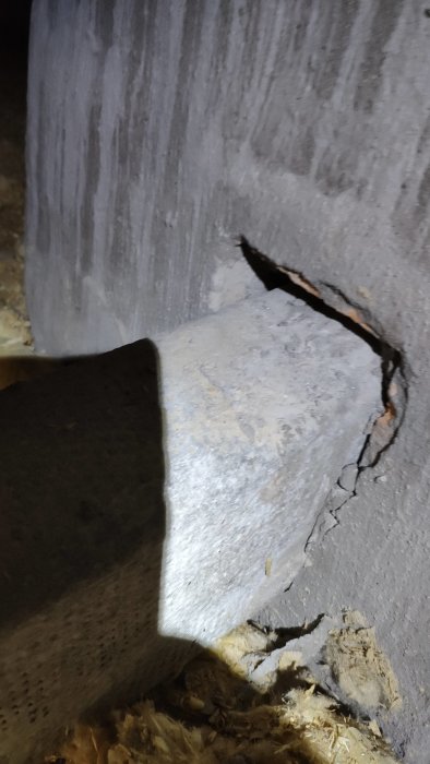 Skadad betongpelare med stort sprucket hål, belyst i mörker, sannolikt strukturell skada.