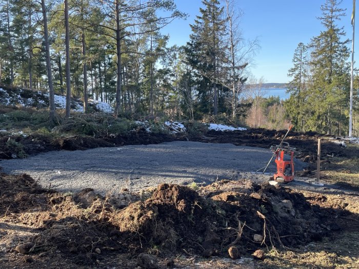 Skogsmark omvandlad till byggarbetsplats, uppgrävd mark, maskiner, med snö och utsikt över vatten.