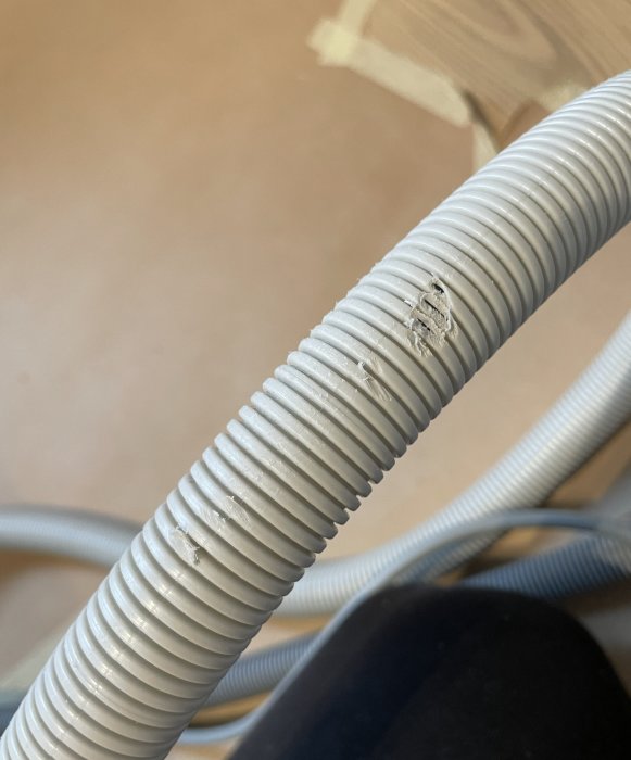 Vit, böjlig rörledning med skada och repor, möjligtvis elektriskt användningsområde, mot suddig bakgrund.