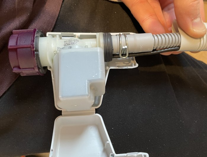 En hand håller en plastmässig apparat med etiketter, möjligen en del av medicinsk eller teknisk utrustning.