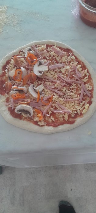 Opreparerad pizza med skinka, ost, tomat, paprika och svamp. Ugnen väntar. Matlagning hemma.