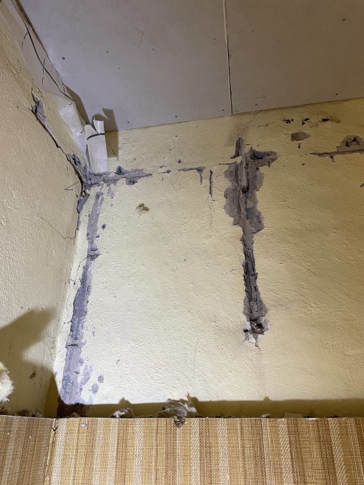 Skadad vägg och tak med sprickor, avskalad färg, fuktskador, och synliga reparationstecken.