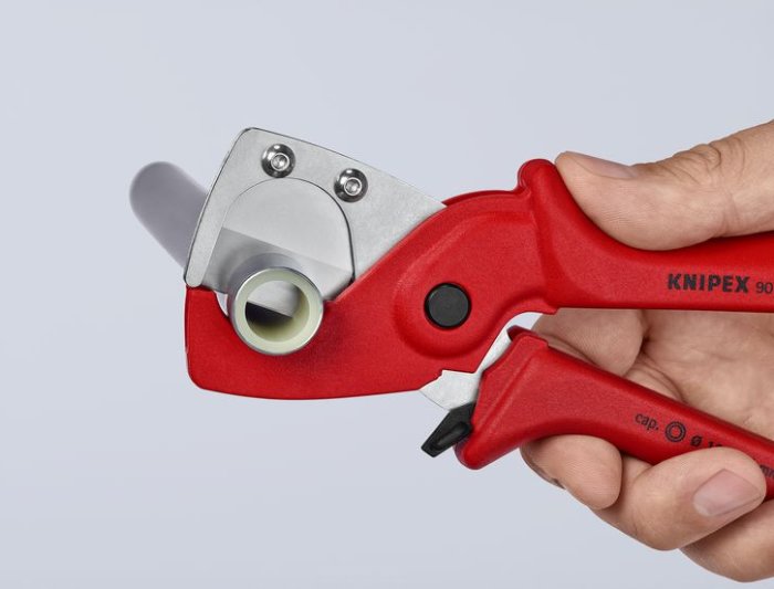 Hand håller röd Knipex-rörskärare mot grå bakgrund, avsedd för klippning av rör.