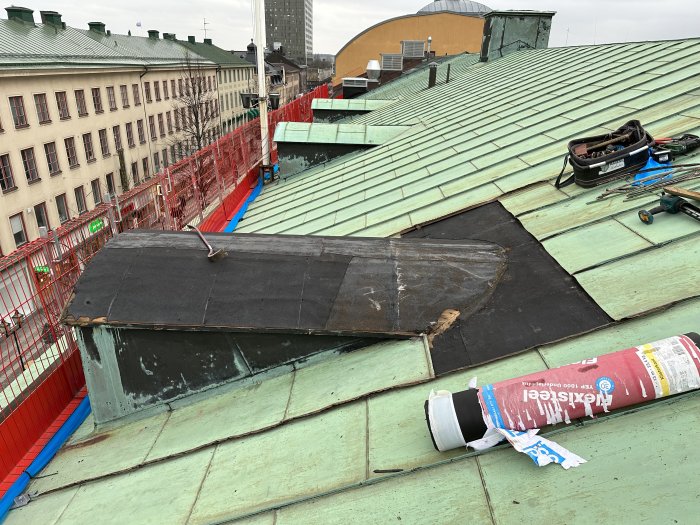 Stadsutsikt, grönt tak under reparation, verktyg, säkerhetsstaket, byggnadsmaterial, övergivet arbetsområde.