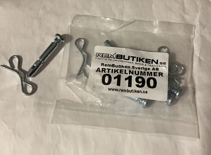 Metallklämma och delar i plastpåse med logotyp och artikelnummer; verktyg eller reservdelar för maskiner eller fordon.