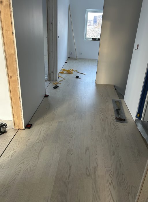 Renovering pågår, trägolv installation, verktyg utspridda, nybygge utanför fönstret, inomhus arbetsmiljö, konstruktionsfas.