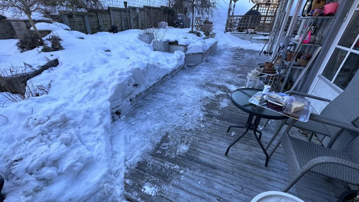 Uteplats med snö, bord med muggar och mat, stolar, bostadsbyggnad, vedtrave, kyligt utomhusmiljö.