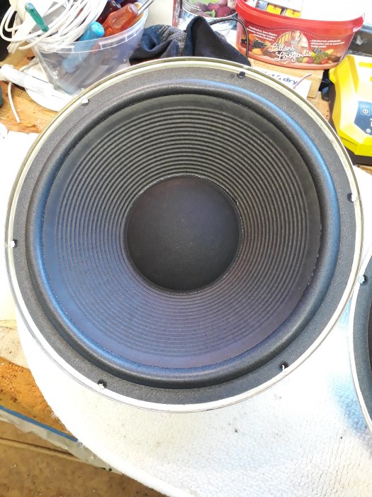 Stor högtalarelement på ett rörigt arbetsbord, sannolikt ett reparation- eller hobbyprojekt.