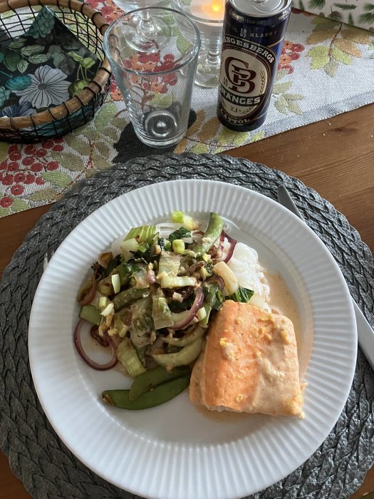 Måltid med lax, sallad, nudlar och öl på ett dukat bord.