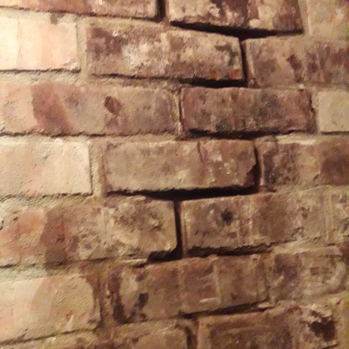 Närbild på texturerad tegelstensvägg med synliga fogar och variation i tegelstenarnas färg och skick.