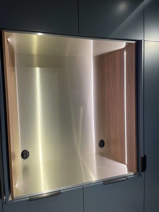 Ett tomt köksskåp med öppna dörrar, av metall och trä, modern design, med handtag.