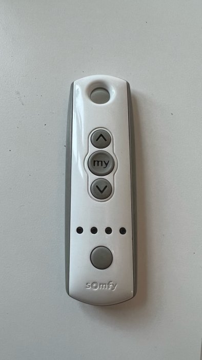 En vit Somfy-fjärrkontroll med tre knappar för upp/ned/my-funktion och fyra programmeringsknappar mot en vit bakgrund.