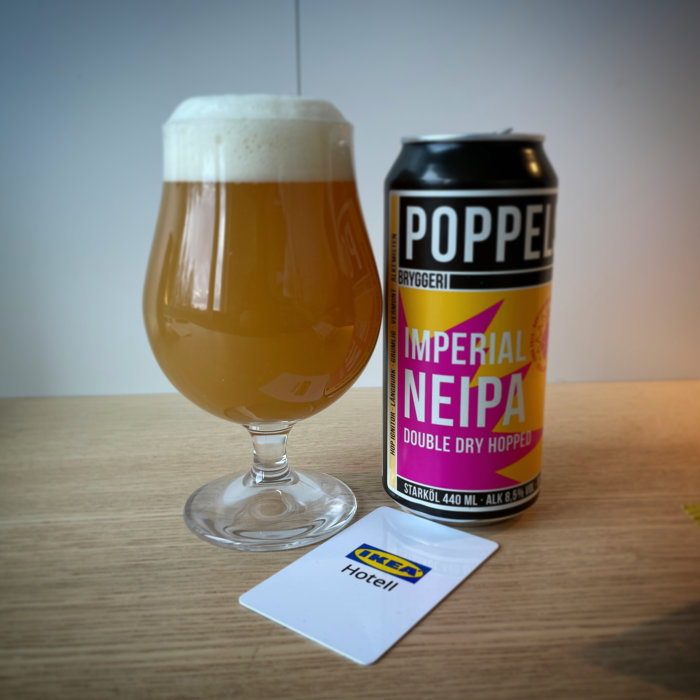 Ett glas öl, ölburk märkt "Imperial NEIPA", IKEA Hotell nyckelkort, enkelt träbord.