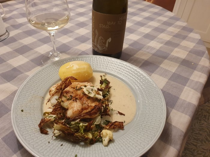 Ett elegant dukat matbord med en tallrik mat, ett glas vitt vin och en vinflaska.