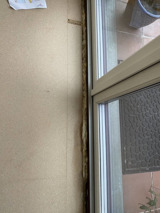 Insidan av ett fönster med synlig isolering och en del av en dörrmatta.