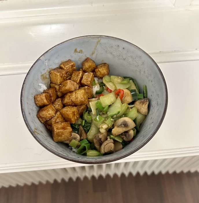 En skål med ris, stekt tofu och blandade grönsaker som pak choi och champinjoner, ser ut som asiatisk mat.
